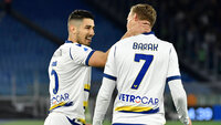 Hellas Verona-Spieler feiern gemeinsam auf dem Spielfeld in weißen Trikots nach einem Tor.